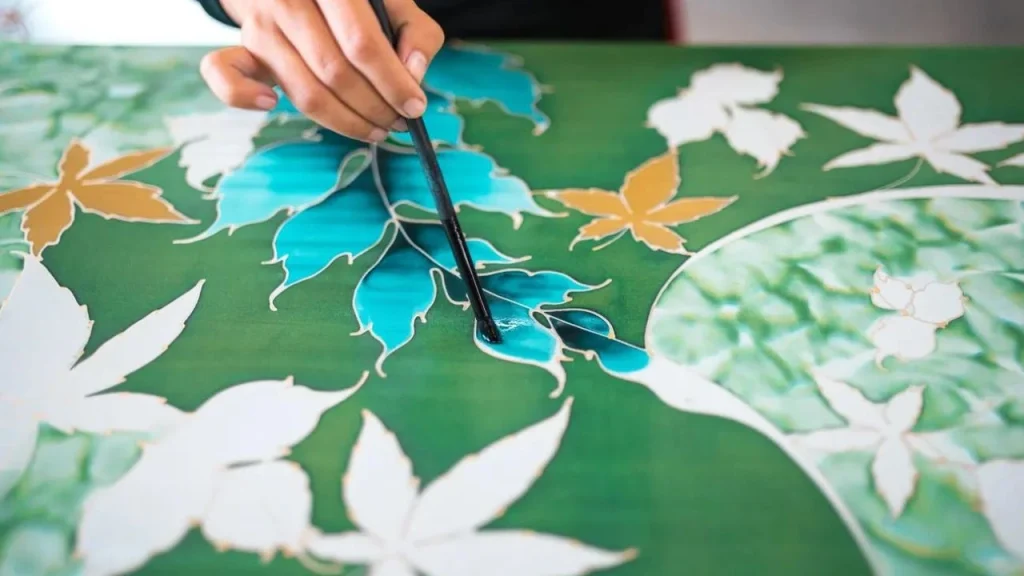 penampakan tangan yang sedang mewarnai batik dengan water colour atau seumpama